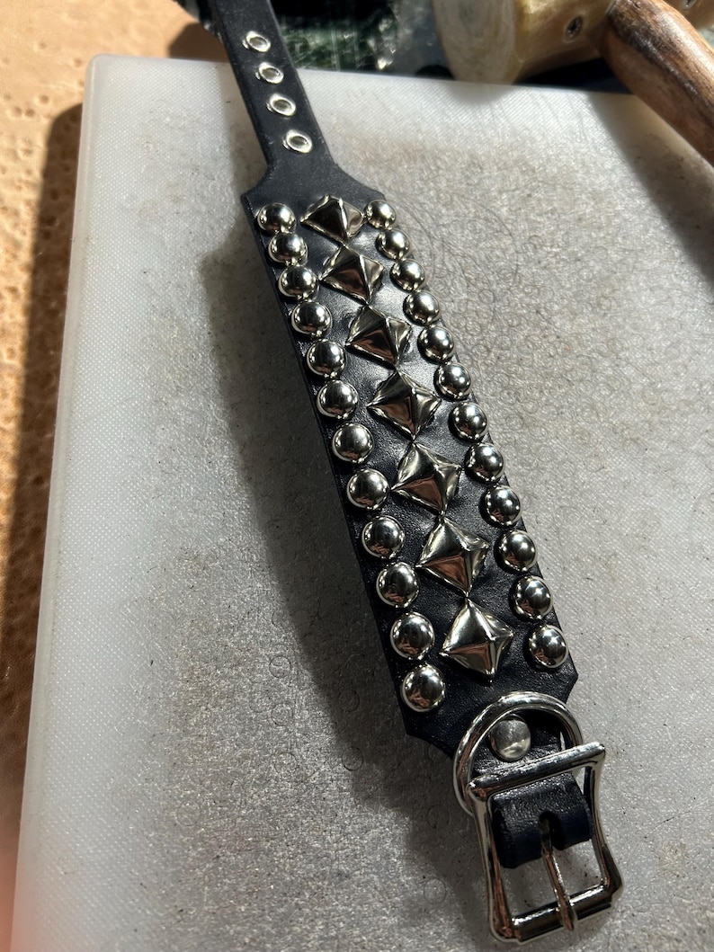 Op de afbeelding: Zwarte leren halsband met zilveren piramide- en ronde studs. De halsband heeft een gespsluiting en meerdere verstelgaten. Het ontwerp toont rijen afwisselende piramide- en ronde studs.