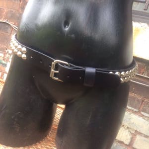May include: A black leather belt with silver pyramid-shaped studs. The belt is worn around the waist of a mannequin.