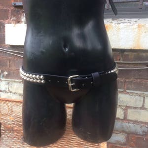 May include: A black leather belt with silver pyramid-shaped studs. The belt is worn on a mannequin.