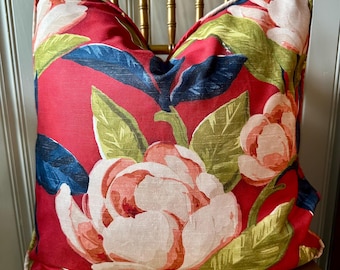 May include: A red pillow with a floral pattern featuring large pink flowers and green leaves. The pillow has a white background and a dark blue outline around the flowers.