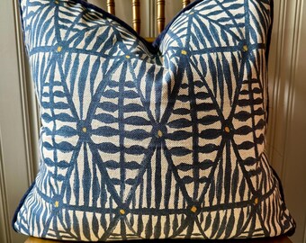 May include: A square decorative pillow with a blue and white geometric pattern. The pillow has a dark blue border and small yellow accents. The pillow is resting on a gold-colored wooden chair.