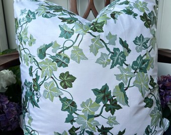 May include: A square white pillow with a green ivy leaf pattern. The pillow is placed on a dark wooden chair. The ivy leaves are in shades of green, creating a natural, botanical design.