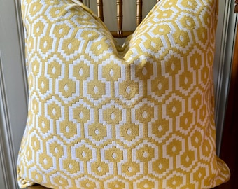 May include: A decorative square pillow with a geometric pattern in yellow and white. The pillow is placed on a wooden chair with a gold finish. The pillow's design features a repeating pattern of interlocking shapes.