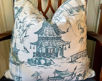 May include: A white pillow with a blue and green pagoda design. The pillow is sitting on a dark blue chair.