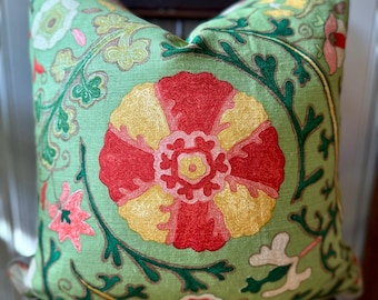 May include: A square throw pillow with a light green base fabric featuring intricate embroidery. The design showcases a large central flower in red and yellow, surrounded by smaller floral motifs, green vines, and leaves in shades of pink, white, and dark green.