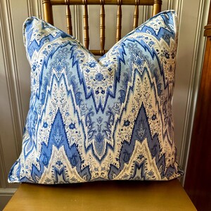 May include: A blue and white patterned throw pillow with a geometric design. The pillow is sitting on a wooden chair.