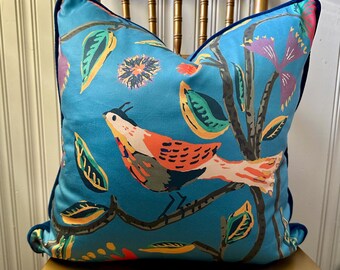 May include: A blue throw pillow with a colorful bird and floral pattern. The pillow has a navy blue trim.