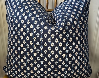 May include: A navy blue throw pillow with a white and light blue floral pattern. The pillow is sitting on a wooden chair.