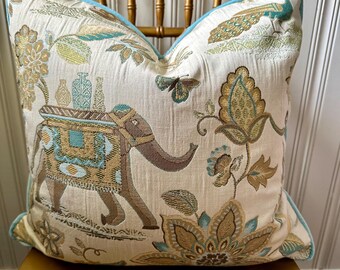 May include: A decorative throw pillow with a cream background and a colorful pattern featuring an elephant, peacocks, and floral designs. The pillow has a light blue border.