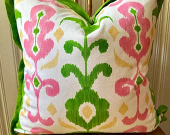 May include: Decorative pillow with a white background and a vibrant floral pattern in pink, green, and yellow. The pillow has a bright green border and is placed on a gold-colored chair.