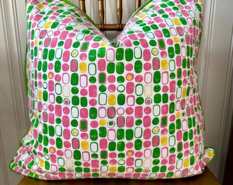 May include: A white pillow with a green, pink, and yellow geometric pattern. The pillow has a green border and is sitting on a wooden chair.