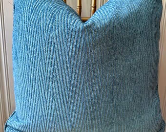 May include: A square, light blue decorative pillow with a textured, chevron-like pattern. The pillow is resting on a wooden chair with a gold finish. The pillow's fabric has a soft, inviting appearance, perfect for home decor.