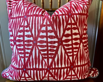 May include: A decorative throw pillow with a red and white geometric pattern. The pillow has a repeating design of red shapes on a white background, with small blue accents. The edges are trimmed with a blue border.
