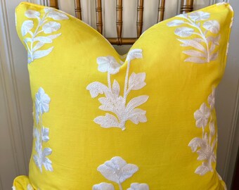 May include: A yellow throw pillow with white embroidered floral designs. The pillow is sitting on a wooden chair.