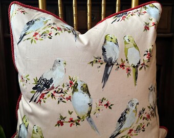 May include: A square decorative pillow with a light pink background featuring a pattern of birds perched on flowering branches. The pillow has a red rope trim.