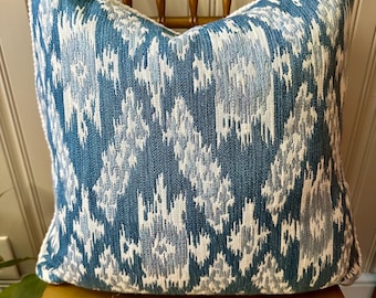 May include: Square decorative pillow with a blue, white, and gray ikat pattern. The pillow is placed on a gold-colored wooden chair. The pillow's design features a textured, woven appearance, adding visual interest to the home decor.