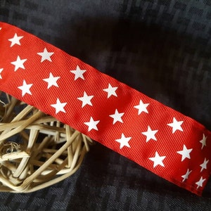 May include: Red ribbon with white stars printed on it. The ribbon is wrapped around a woven ball.