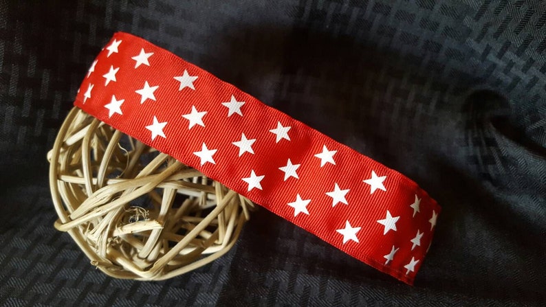 May include: Red ribbon with white stars printed on it. The ribbon is wrapped around a woven ball.
