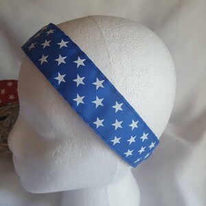 May include: A blue headband with white stars printed on it. The headband is made of fabric and is worn on a white mannequin head.