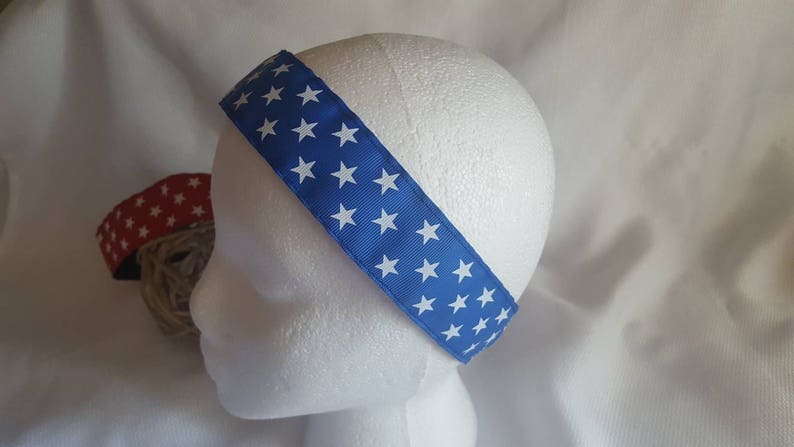 May include: A blue headband with white stars printed on it. The headband is made of fabric and is worn on a white mannequin head.