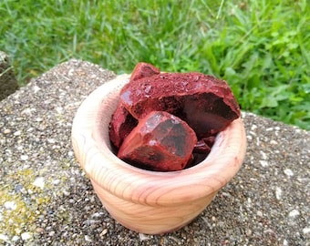 May include: A wooden bowl filled with dark red chunks. The bowl is made of light-colored wood and has a rounded shape. The background is a mix of green grass and a concrete surface.
