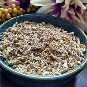May include: A teal ceramic bowl filled with light brown, shredded plant material. The bowl has a dark green rim and sits on a dark wooden surface. Decorative flowers and berries are in the background.