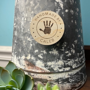 May include: A round wooden tag with the text "Handmade by Caleb" and a handprint design.