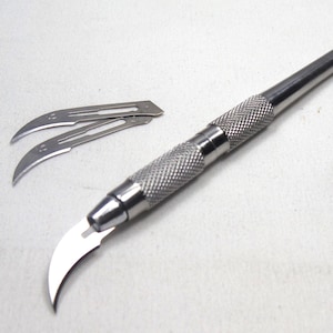 May include: A silver surgical scalpel with a curved blade and a silver handle. Three extra blades are included.