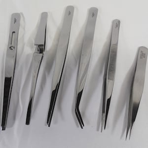 Puede incluir: Conjunto de siete pinzas de acero inoxidable con diferentes estilos de punta. Las pinzas son todas de color plateado y tienen un acabado pulido.
