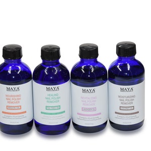 May include: Four blue glass bottles with black caps containing nail polish remover. Each bottle has a label with the brand name "MAYA" and a description of the type of nail polish remover, including "Nourishing", "Healing", "Revitalizing", and "Moisturizing".