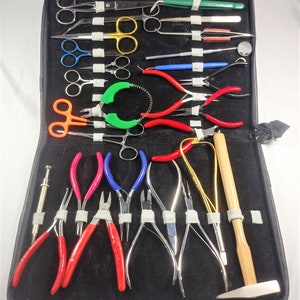 May include: A black case with a variety of jewelry making tools, including pliers, cutters, tweezers, and a hammer. The tools are arranged in rows and are held in place by white tape.
