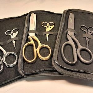 Puede incluir: Cuatro pares de tijeras en estuches de cuero negro. Las tijeras son de diferentes colores y estilos, incluyendo oro, plata y negro.