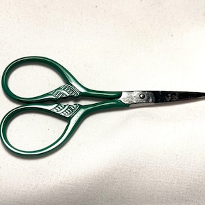 May include: Green handled scissors with a silver blade. The handles have a decorative pattern.