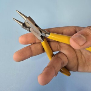 May include: Round-nose pliers featuring a polished stainless steel head with two tapered, conical jaws and bright yellow rubberised handles. The metal joint area is clearly marked with the text Stainless Steel and Pakistan.