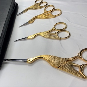 May include: Set of four gold-colored, bird-shaped scissors with a black leather case. The scissors have intricate details and are ideal for crafts or sewing.