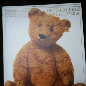 May include: The Teddy Bear Encyclopedia book cover features a brown teddy bear sitting with its paws crossed. The book title is "The Teddy Bear Encyclopedia" and the author is Pauline Cockrill with a foreword by Paul & Rosemary Volpp.