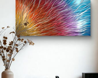 May include: Abstract metal wall art with a vibrant color gradient. The artwork transitions from yellow to orange, red, purple, and blue. Silver lines flow across the surface, creating a textured effect. The piece is mounted on a white wall.