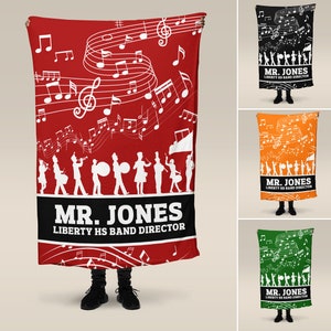 May include: A red fleece blanket with a musical theme. It features white musical notes and a marching band silhouette. The text "MR. JONES LIBERTY HS BAND DIRECTOR" is printed at the bottom.