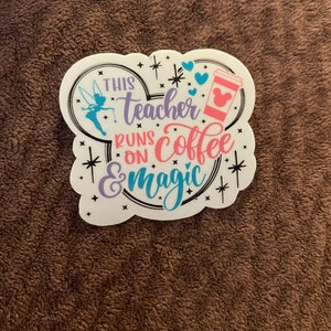 May include: White sticker with a Mickey Mouse head shape. The sticker has a Tinkerbell fairy, hearts, stars, and a coffee cup with a Mickey Mouse ear lid. The text reads "This teacher runs on coffee & magic".