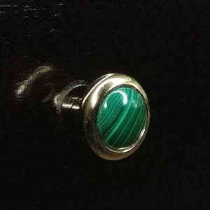 Könnte beinhalten: Nahaufnahme eines runden, silberfarbenen Knopfes mit einem grünen Malachit-Edelstein. Der Knopf ist auf einer schwarzen Oberfläche montiert.