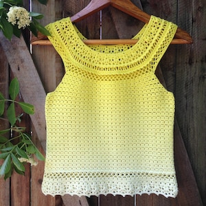 May include: A yellow crochet tank top with a white crocheted trim. The top has a wide, crocheted neckline.