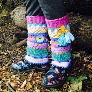 May include: Colorful crocheted leg warmers with a pink, yellow, blue, and green color scheme. The leg warmers are worn over black boots with a floral print.