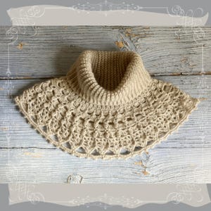 May include: A crocheted beige cowl with a delicate lace pattern and a high, folded collar.