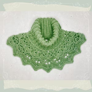 Può includere: Un collo all'uncinetto fatto a mano, verde chiaro, con un design a collo alto. Il collo presenta un bordo smerlato e un motivo a pizzo traforato. Il filato ha un aspetto morbido e strutturato. L'articolo è esposto su uno sfondo neutro.