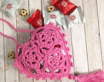 Puede incluir: Una bolsa de corazón de crochet rosa con un borla rosa. La bolsa está llena de pequeños corazones de caramelo que dicen "With Love" y "White Love".
