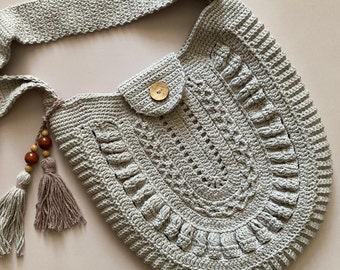 May include: A crocheted gray shoulder bag with a wooden button closure and tassels. The bag has a unique design with a scalloped edge and a textured pattern.