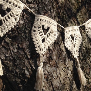 May include: A white crocheted garland with heart-shaped cutouts and tassels hanging from a tree trunk.