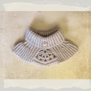 May include: A gray crocheted collar with a pearl button in the center. The collar has a delicate lace pattern around the edges.