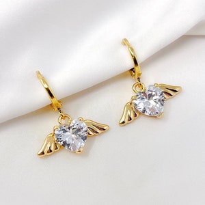 May include: Gold hoop earrings with a dangling heart-shaped crystal accented with gold wings.