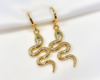 May include: A pair of gold snake earrings with green gemstone eyes. The snakes are coiled and have a detailed design.